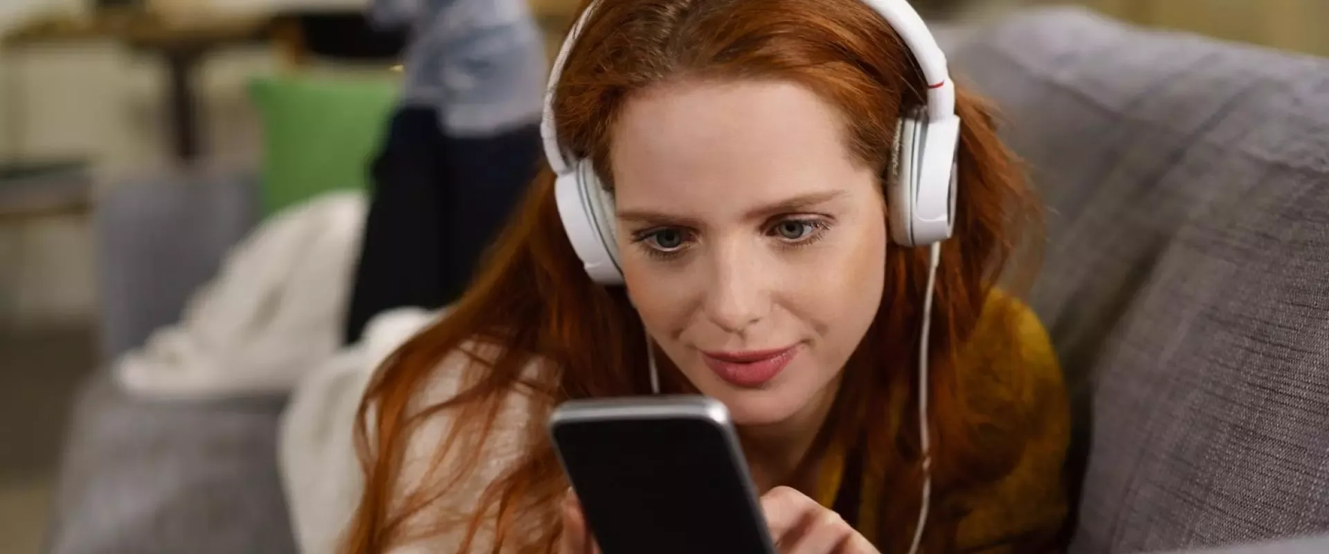 Frau mit Kopfhörern und Handy auf dem Sofa