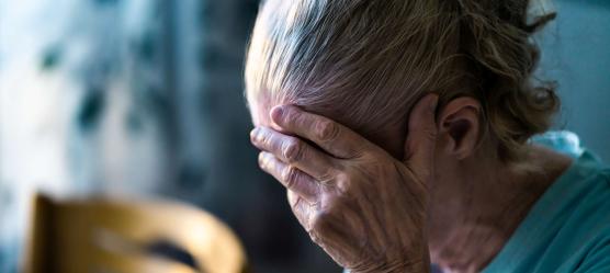 Ältere Frau mit gesenktem Kopf und ihre Hand vor ihr Gesicht haltend.