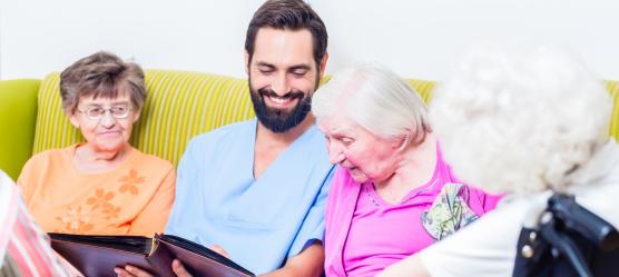 Pfleger sitzt mit Seniorinnen auf einem Sofa